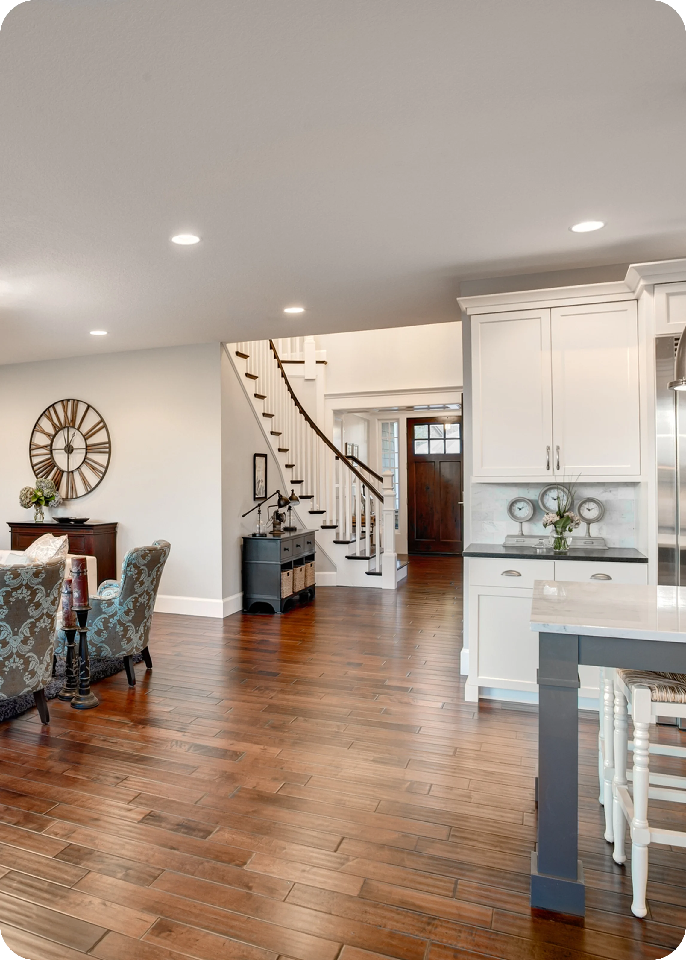 Modern living area with hardwood floors, white cabinetry, and a spiral staircase. Large wall clock and seating are visible, along with a glimpse of the front door.
